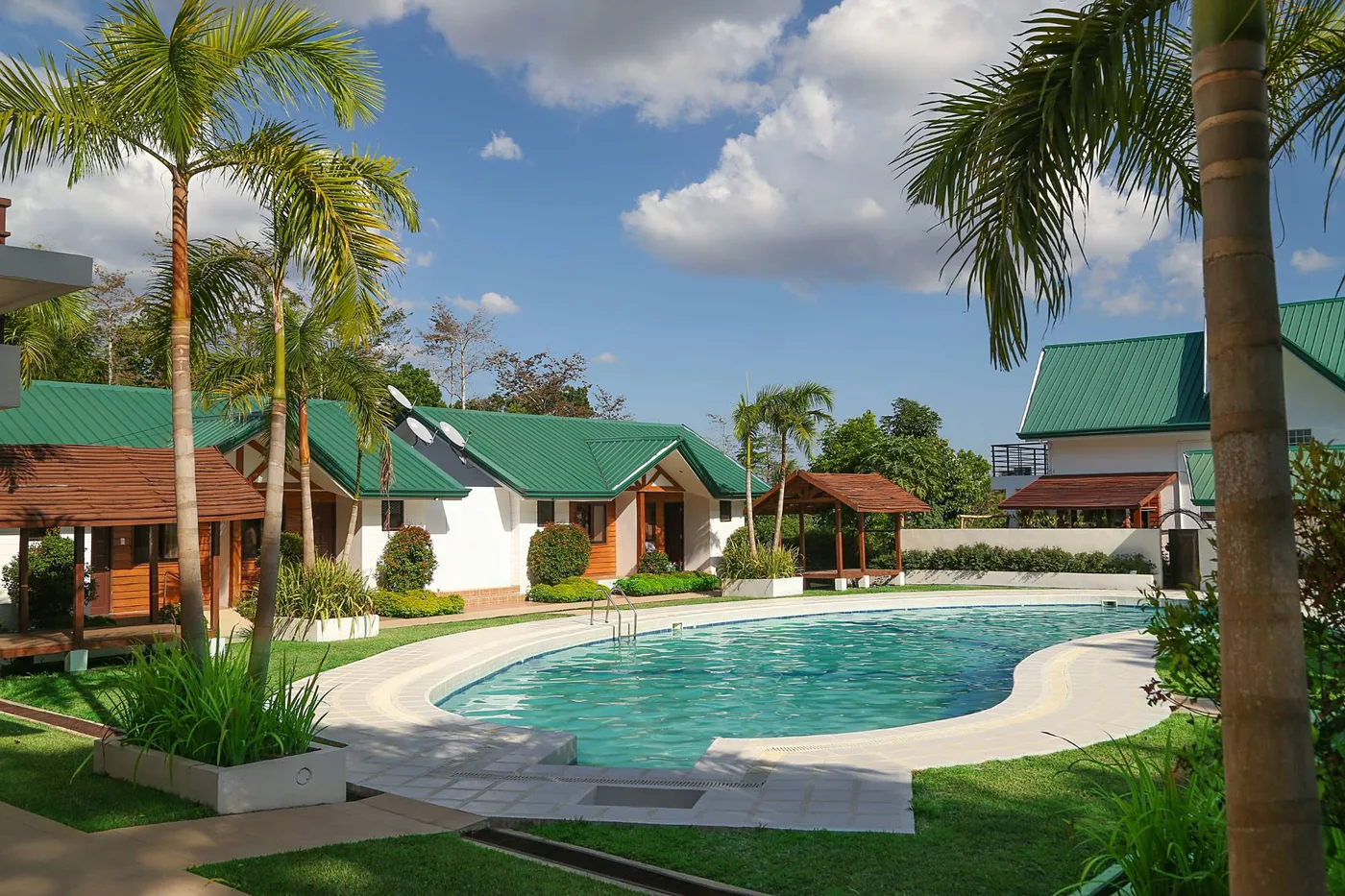 The swimming pool among palm trees and green-roofed guest cottages